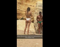 Girl white bottoms takes photo for buff guy on rock green speedo