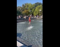 Shirtless man fan dance at public fountain