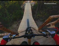 BMX biker jumps off wooden ramp and dock, races down trail