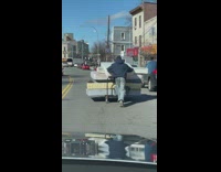 Guy pushes a trolley with 5 mattresses on it on the road 
