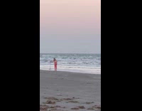 Woman in pink top bikini poses with tripod on the beach