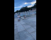 Woman sits near fountain while man pictures