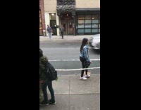 Woman rolls a giant yarn ball down the sidewalk, people hold loose yarn and follow
