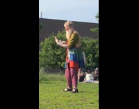 Old man in colorful boho clothes stands in the middle of a park and plays with crystal ball