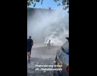 Guy standing in the street getting drenched with a broken fire hydrant