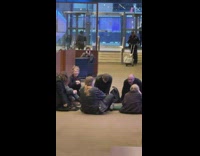 Group of People Sing while Seated on Lobby Floor