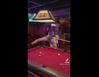 Guy purple shirt with puppy carrier on playing pool