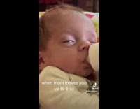 Baby drinks milk bottle with eye slightly open 