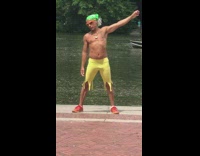 Man in yellow short and green bandana stretches his arms at the park near pond