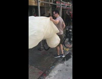 Guy holds white inflatable penis used for statue and parks bike on sidewalk