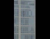 Worker sitting on window ledge to clean window of tall building
