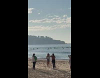 Woman white top throws plastic bottles upwards at the beach