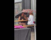 Two women enjoy drinks outside during rain umbrella
