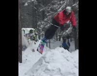 Guy skis down mountain off tall ramp and does a scorpion in the snow