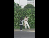 Girl sweater hold bag beside grass wall 