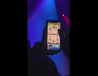 Guy in crowd at concert plays mobile game while people cheer watching