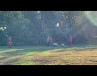 Two people wearing jumpsuits and holding balloons film video 
pt. 2