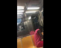 Man in pink shirt and pants cuts braided hair with scissors on the subway