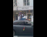 Guy wearing spiderman costume drinks on car roof 