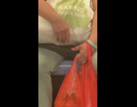 Woman holds bag that says Say no to plastic bags and also holds two orange plastic bags on subway train