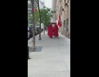 People wearing long red garments walk sidewalk