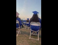 People sit in chairs on grass at graduation