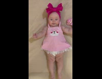 Baby on bed in dress and headband swinging arms and legs
