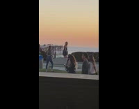 Girl stand on bench guy photobombs pier sunset