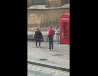 Woman takes picture next to red telephone booth 