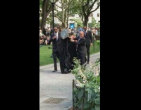 Men in tuxedos chauffeur person in black cloak and circle mask 