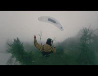 Brown jacket guy floats down white parachute 