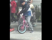 Man sit on pink kiddie bike street