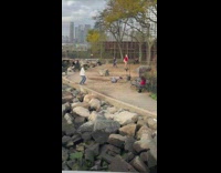 Man in white jacket tiktok dance near some rocks at the park
