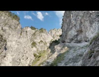 Man kicks down rock at top of mountain wall