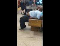 Man sits on edge of seat with belly out and thrusts the air in subway station