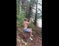 Guy blue shorts swings off tree rope and bellyflops into lake water