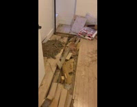 man shows torn up floor in apartment