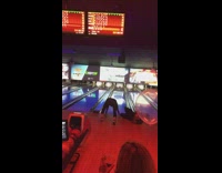 Guy slides on floor ad records girl throwing bowling ball down lane