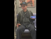 Man holds out phone playing music video and wears marquee hat that says God does not exist