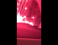 man lights red firework in front of car