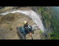 Black shirt guy sits mountain top by waterfall 
