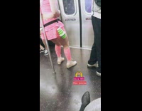Man wears pink shirt, skirt, and knee high socks, shakes butt on subway pole