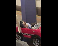 Two chihuahuas wearing blue sunglasses sit inside red mini cooper toy car inside subway station