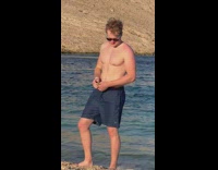 Man shirtless with sunglasses poses by the beach