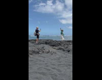 Woman hat teal shirt dance on rock beach