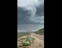 Tornado forms on the cloudy sky and slowly approaches the road