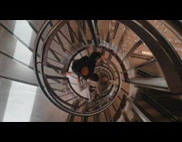 Two guys slide down spiral stair railing