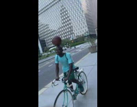 Guy balances ball on his head while on a bike 