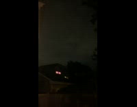 Continuous lightning flicker in sky behind house