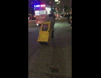 Guy drags yellow newspaper box down sidewalk